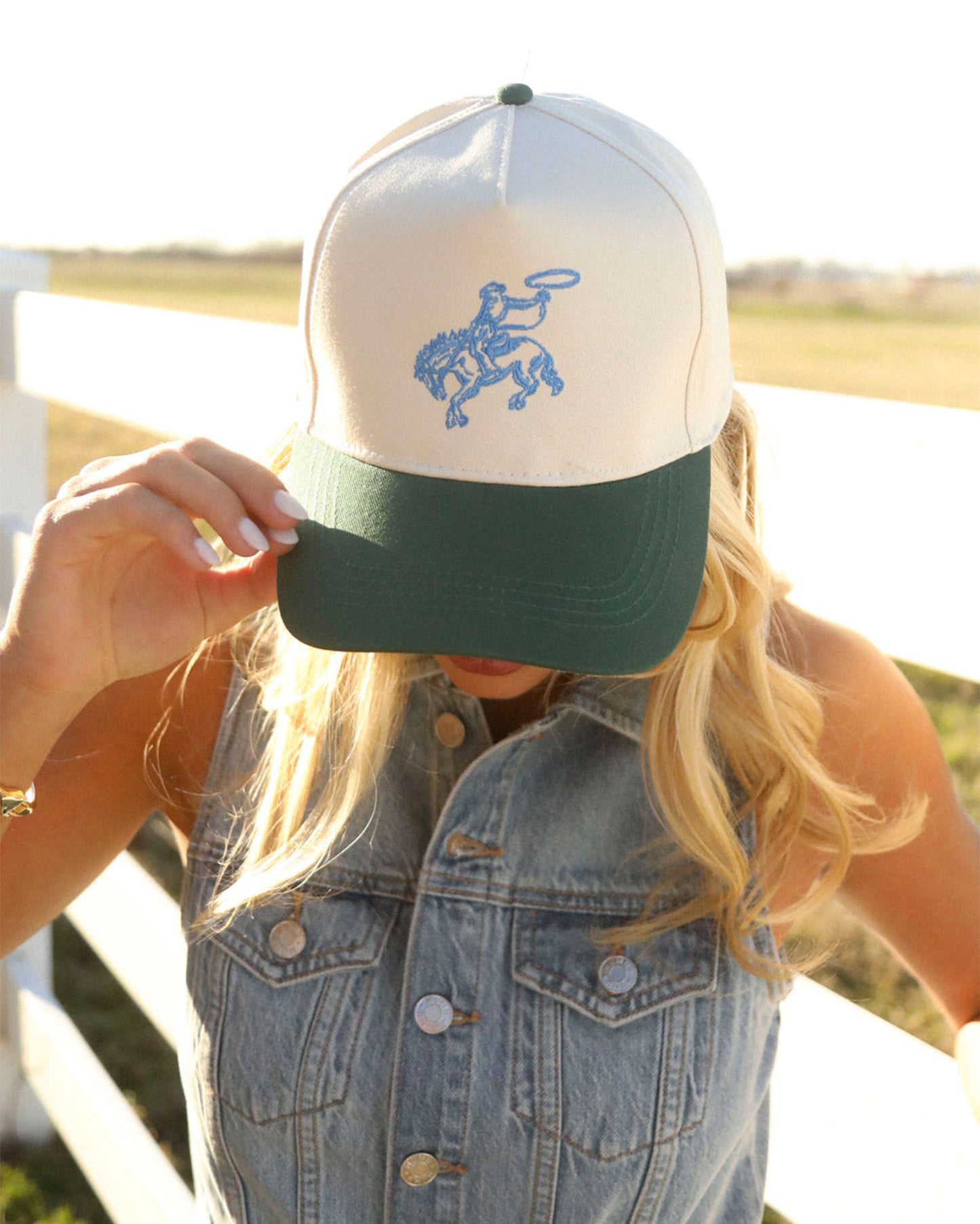 Close-up of the Women's Rodeo Rider Trucker Cap by Charlie Southern being worn by a woman, showcasing the embroidered cowboy design against a clear sky.